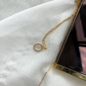 Detailed close-up of a vintage oval white gemstone pendant with a gold chain on white fabric