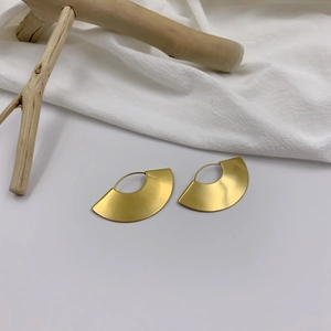 Detail view of gold fan-shaped geometric earrings with matte finish on white linen fabric