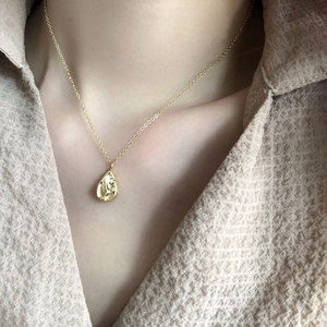 Détail d'un collier pendentif goutte d'or avec texture de lave sur un mannequin