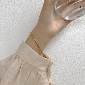 Close-up of a double-layered gold snake bone chain bracelet worn with a beige shirt
