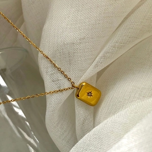 Gold titanium necklace with rectangular starburst pendant on white linen background