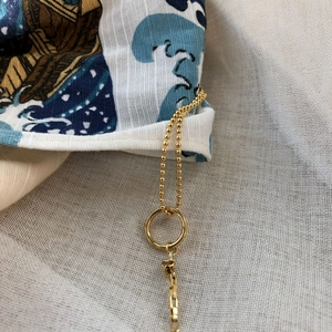 Elegant gold ball chain necklace featuring asymmetric rings on a textured fabric backdrop