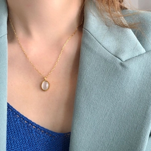 Close-up of golden oval necklace with white gemstone on model wearing a blazer