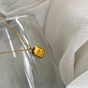 Detail of gold titanium necklace featuring a rectangular starburst pendant with crystal