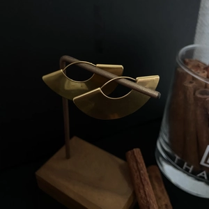 Polished gold semi-circle earrings displayed on a minimalist wooden stand detail