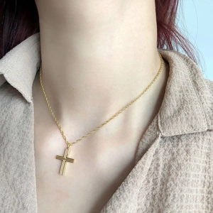 Close-up of minimalist gold cross necklace worn by model on beige textured fabric
