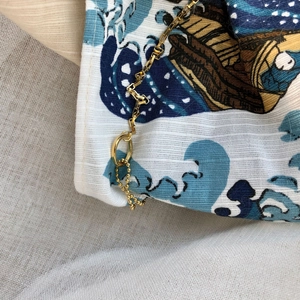 Macro detail of wave print canvas pouch featuring elegant gold metal chain strap