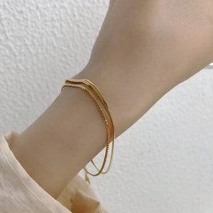 Minimalist double layer gold snake chain bracelet for women on a textured background