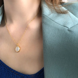 Close-up of elegant gold oval pendant with white opal stone on female model neckline