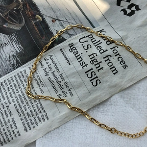 Minimalist gold chain necklace with oval links layered on textured white fabric background