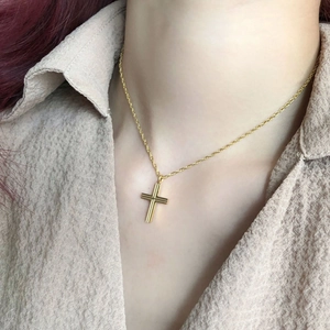 Macro detail of golden cross necklace with vertical stripes on rope chain worn by model