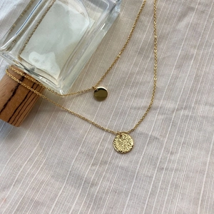 Zweischichtige Goldkette mit glatten und gehämmerten runden Anhängern auf Leinenstoff