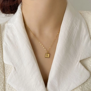 Détail du collier carré en titane doré avec gravure de rose sur une chaîne chic