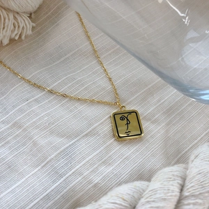 Détail du collier chaîne dorée avec art facial abstrait sur pendentif rectangle sur tissu