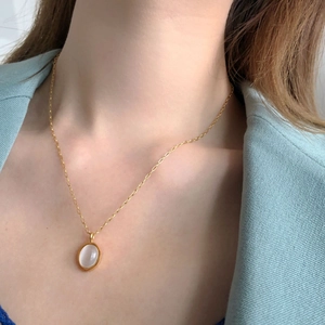 Close-up of elegant gold necklace with oval white gemstone worn by model in green suit