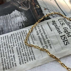 Gold paperclip chain necklace with rectangular links on vintage newspaper background