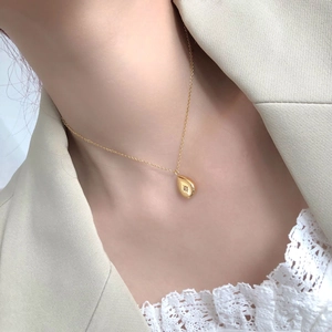 Detail of gold water drop necklace with starburst engraving and zircon on a female model