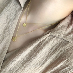 Detail von geschichteten goldenen Münzhalsketten mit Hammerschlag und glattem Finish