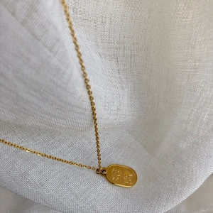 Détail du collier pendentif ovale doré avec caractères chinois gravés pour la paix