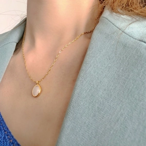 Close-up of golden oval necklace with white inlay worn over a blue blazer