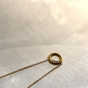 Détail macro du pendentif cercle doré avec fine chaîne croisée sur tissu blanc