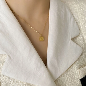 Gros plan du collier doré avec pendentif carré rose sur une veste en tweed