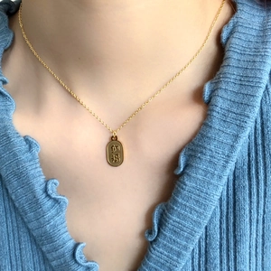 Détail du collier chaîne dorée avec pendentif ovale et gravure chinoise de chance