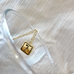 Détail du pendentif carré doré avec gravure de visage artistique sur chaîne minimaliste
