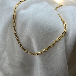 Detailed view of a golden paperclip chain necklace on white textured fabric background