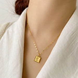 Gros plan d'un pendentif carré doré avec relief de rose sur une chaîne délicate