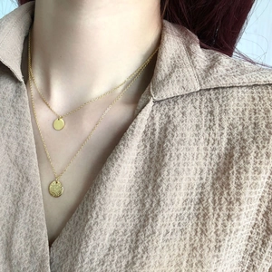 Detail einer goldenen Schichtkette mit glattem Plättchen und gehämmerte Rundanhänger