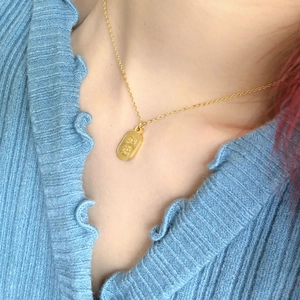 Collier minimaliste en or avec pendentif Nafu porté sur un haut en tricot bleu
