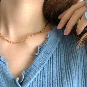 Detail of polished gold paperclip link chain necklace on model with blue ribbed sweater