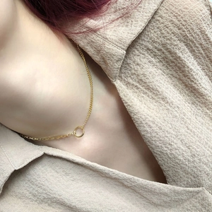Close-up of asymmetric gold necklace with beads and link chain on a beige shirt