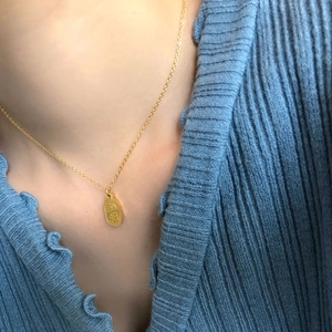Détail d'un collier doré avec pendentif ovale Ping An sur un pull bleu tricoté