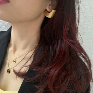 Detail of geometric fan earrings and double-layered gold necklace with Good Luck pendant