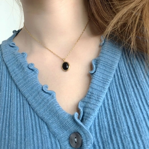 Close-up of vintage oval black agate pendant necklace worn with a blue cardigan