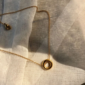Gros plan d'un collier avec pendentif cercle doré brillant sur tissu de lin blanc