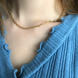 Close-up of golden paperclip chain necklace on a model wearing a blue knitted sweater
