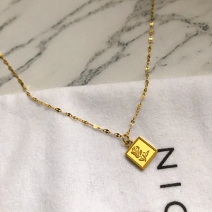 Vue macro détaillée d'un pendentif carré doré avec rose gravée sur une chaîne élégante