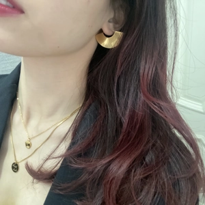 Close-up of gold semi-circular earrings and layered necklace with Good Luck pendant
