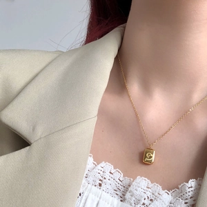 Detailed shot of a gold titanium necklace featuring a rectangular embossed pendant with a small zircon