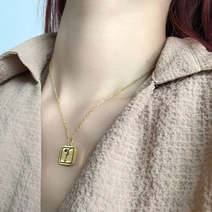 Détail d'un collier doré avec pendentif visage porté sur une chemise beige texturée