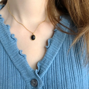Vintage gold necklace with oval black agate pendant worn on a model in blue knitwear