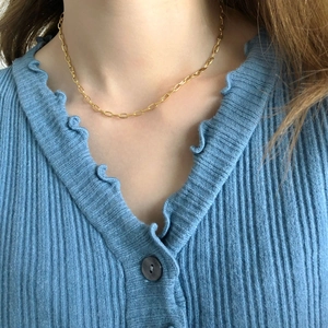Close-up of gold paperclip link necklace worn on model with blue knit sweater