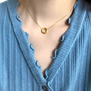 Gros plan d'un collier doré avec pendentif cercle sur fond de pull en tricot bleu