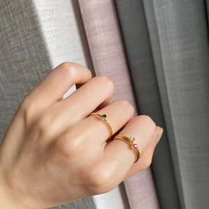 Close-up of thin 14k gold-plated rings with emerald and ruby gemstones on finger