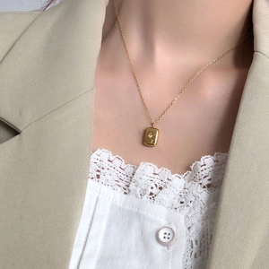 Detail of gold titanium necklace featuring a starburst rectangle pendant on a model