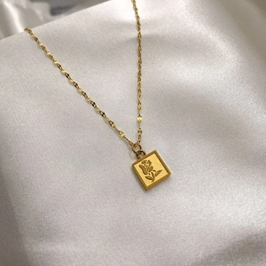 Gros plan d'un pendentif doré rectangulaire avec relief rose sur soie blanche
