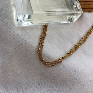 Macro shot of minimalist gold layered beaded chain on white linen with glass decor
